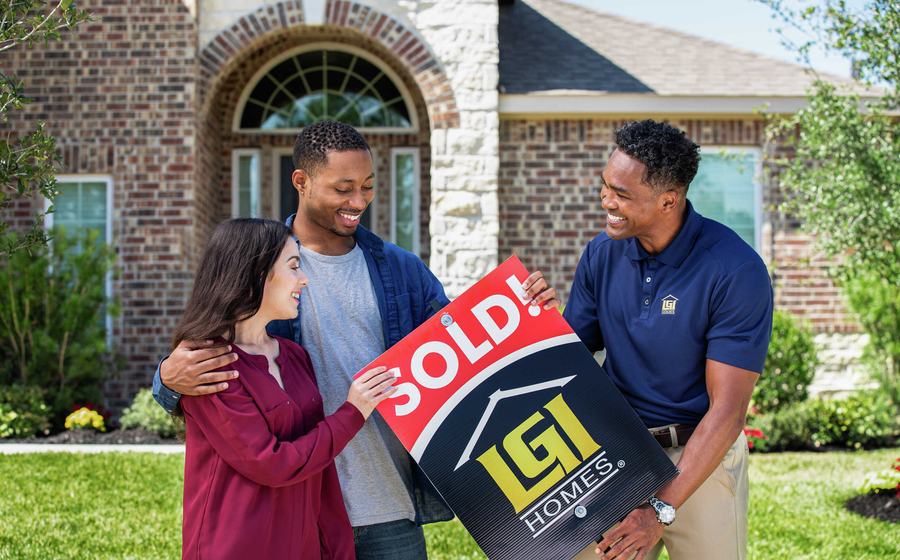 New Home Sales Consultant standing in front of a new-construction home with happy customers holding a sold sign.