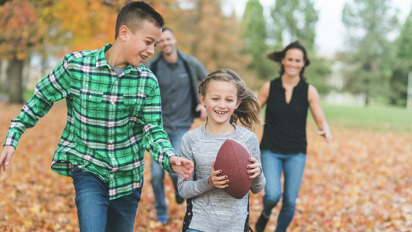 Stock image of family at park playing football in fall leaves.