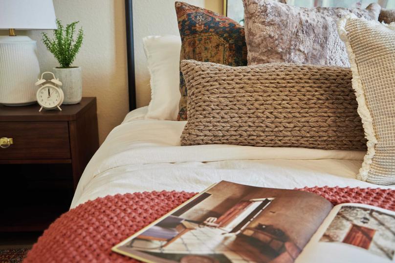 This bedroom has been staged with gorgeous white and rust colored bedding, an abundance of accent pillows, and a wood end table.