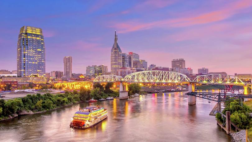 Nashville, Tennessee Downtown skyline at evening time taken from the Cumberland River showing a riverboat, bridge, and skyscrapers with lit windows