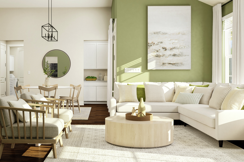 Rendering of living room area showing a
  white sectional couch along a green accent wall and large windows, a coffee
  table, accent chairs, and a view of the kitchen and dining space in the
  background with dark wood look flooring throughout.