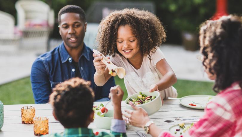 A girl serves salad to her family at the dinner table.