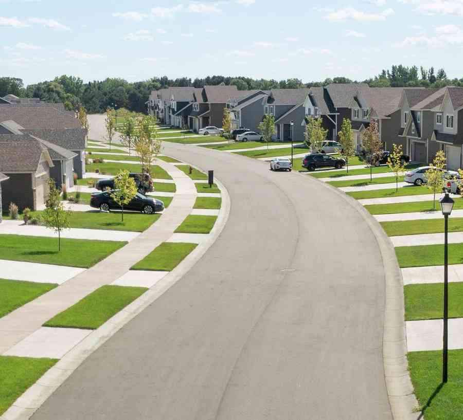 Aerial photo of neighborhood street with sidewalks and green lawns, blue sky.
