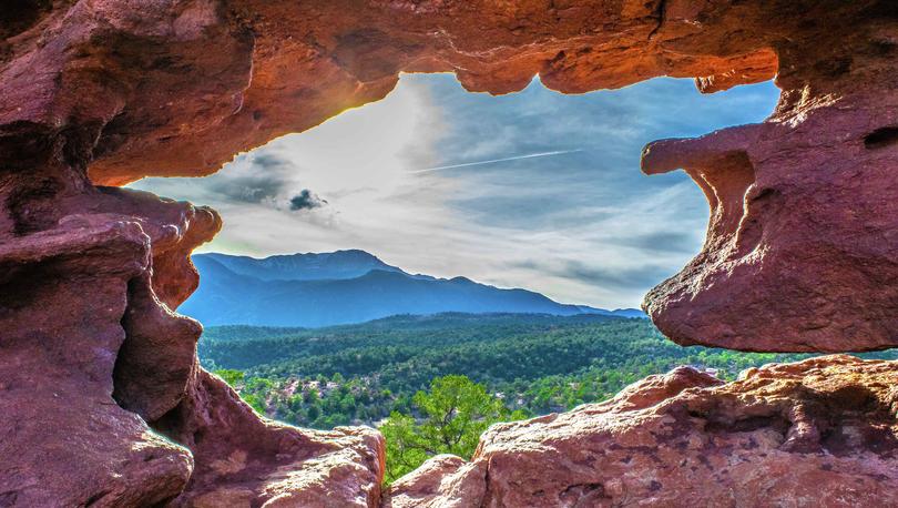 Colorado Springs, CO Garden of the Gods hole in the rock with green trees and blue mountains in the distance