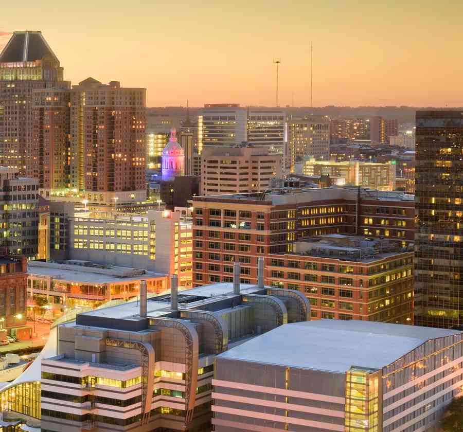 Baltimore, Maryland Inner Harbor and downtown Skyline showing numerous building's windows lit up and the sun setting in the horizon