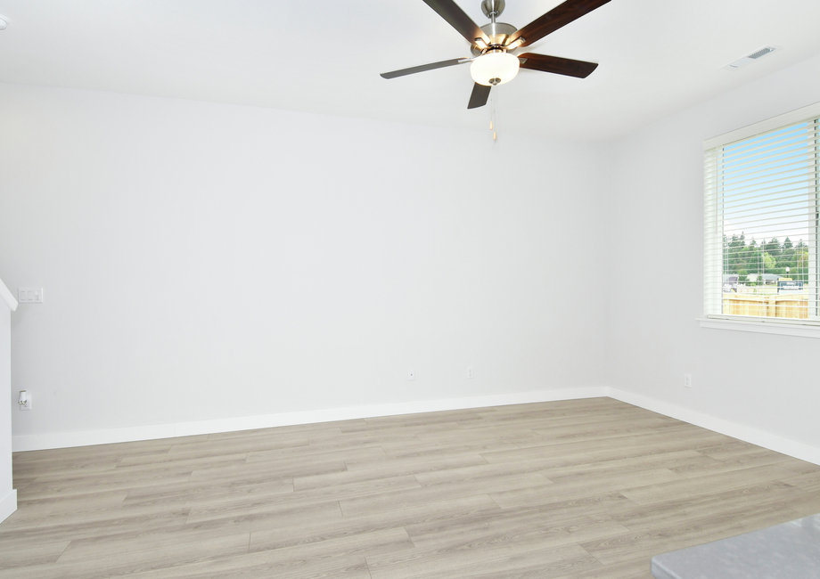 The family room is spacious with plank and a ceiling fan.