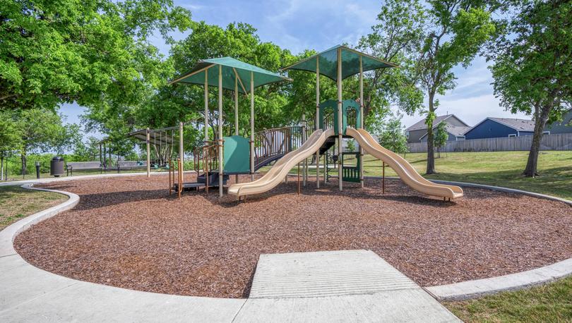 Children's playground with slides and swings, surrounded by trees and walking trails. 