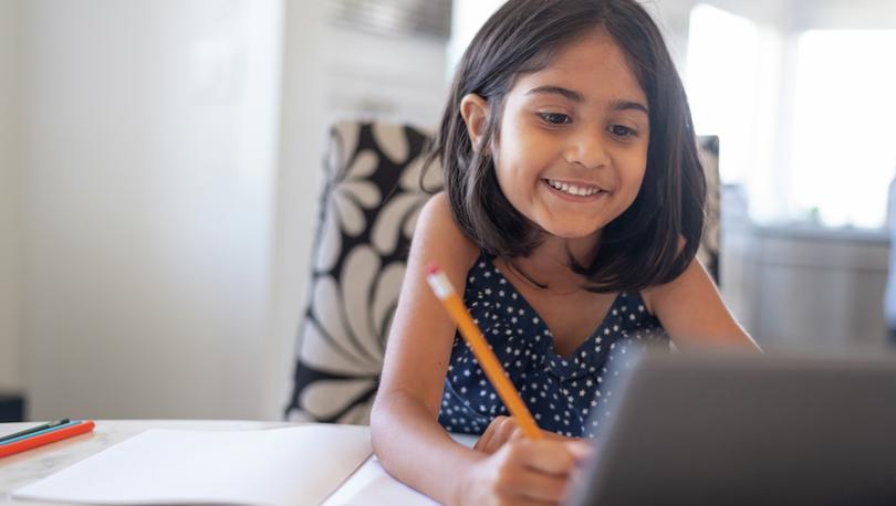 Stock photo of a cute elementary age girl using a laptop computer while attending school online.