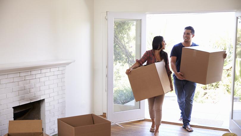 A young couple carries moving boxes into their new home.