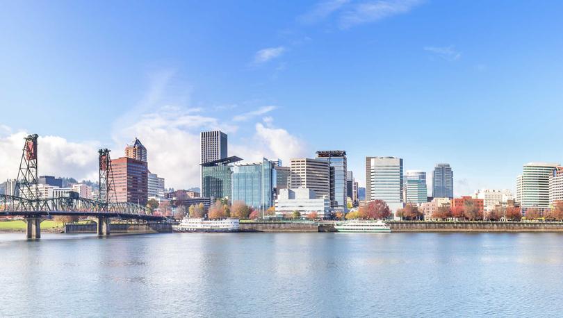 Portland, Oregon cityscape showing calm waters, railbridge, and numerous skyscrapers in the distance