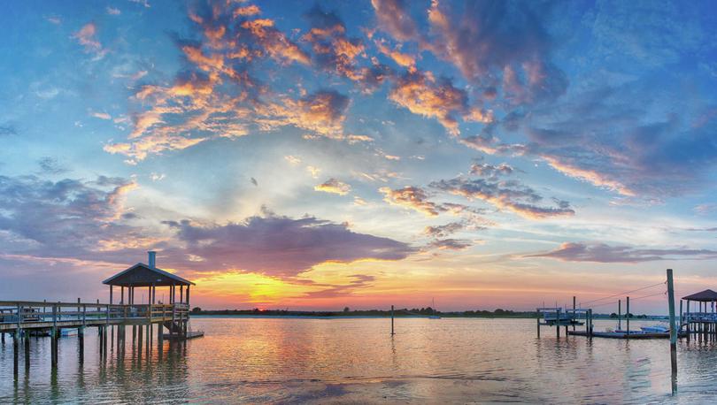 Wrightsville Beach, NC Banks Channel at sunset with cloudy skies, wooden pier, and rolling surf