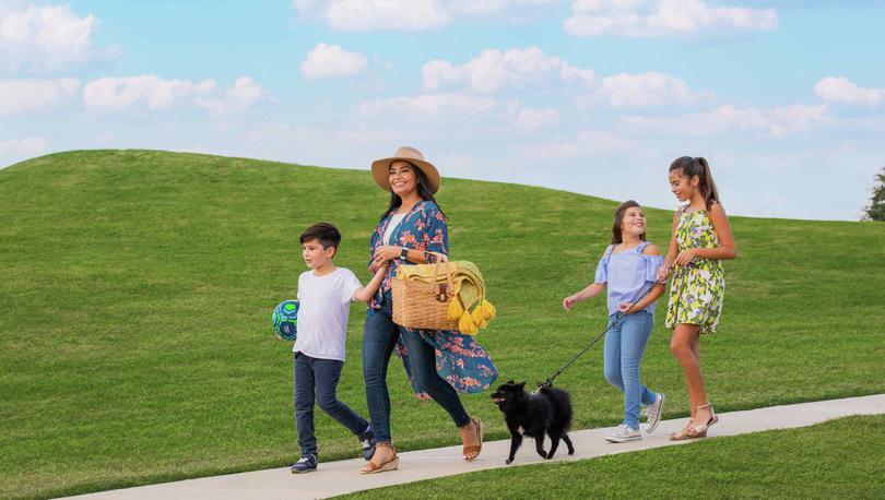 A family walking through the beautiful walking trails of a neighborhood with a picnic basket and their dog. 
