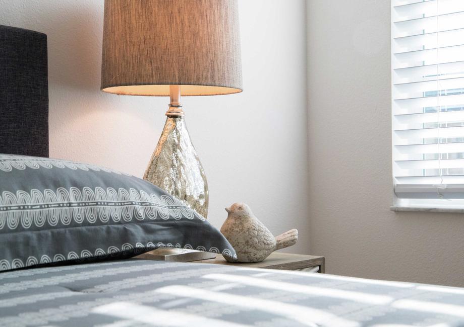 Bedroom completed with patterned beddings, dark wood headboard and shiny lamp with beige shade.