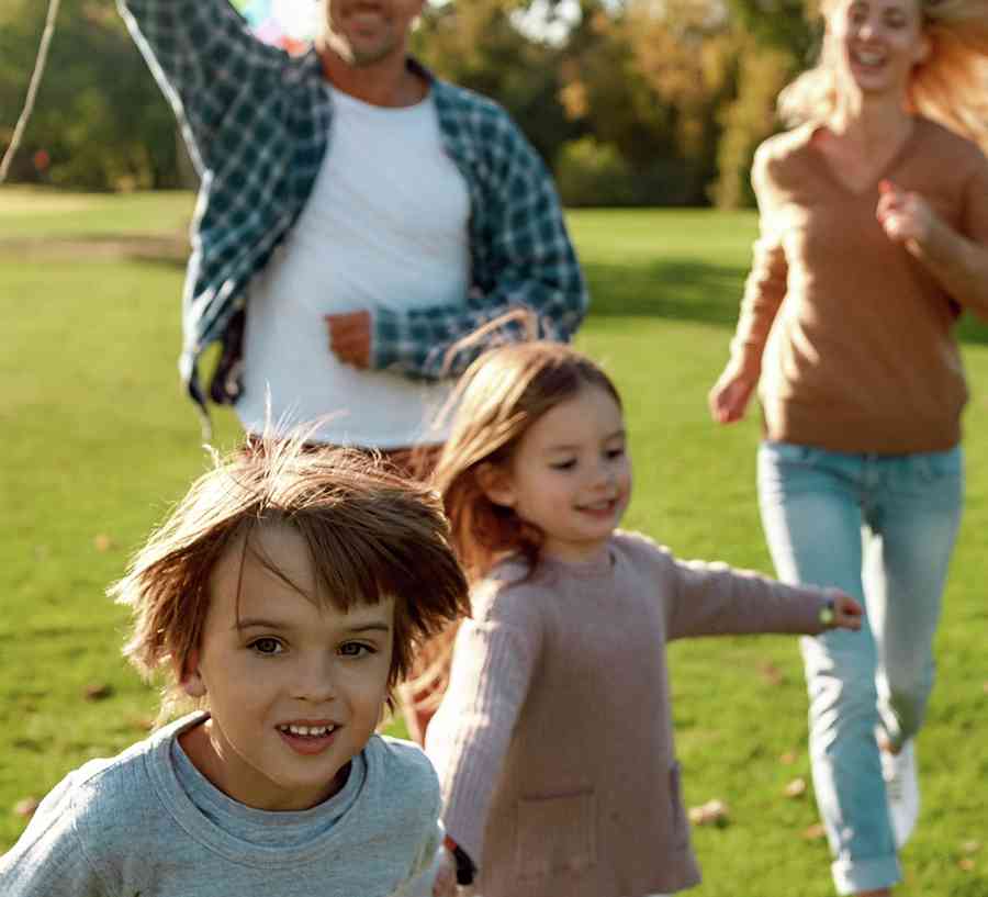 Family running in a field with a kite on a sunny day.