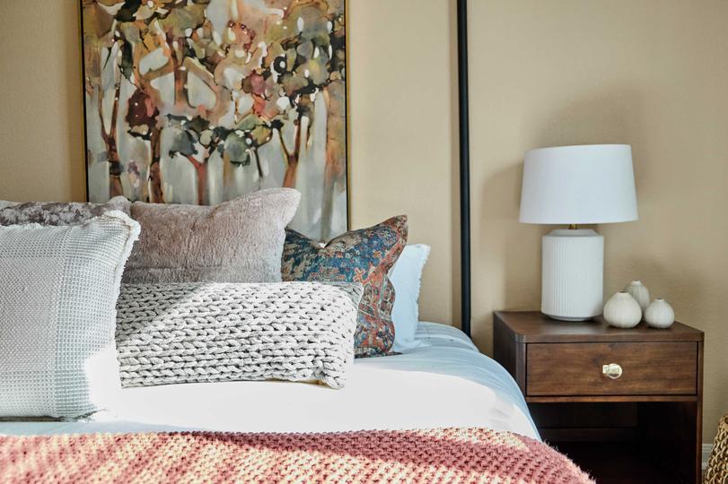 Bed with pink and tan linens and side table with a white lamp