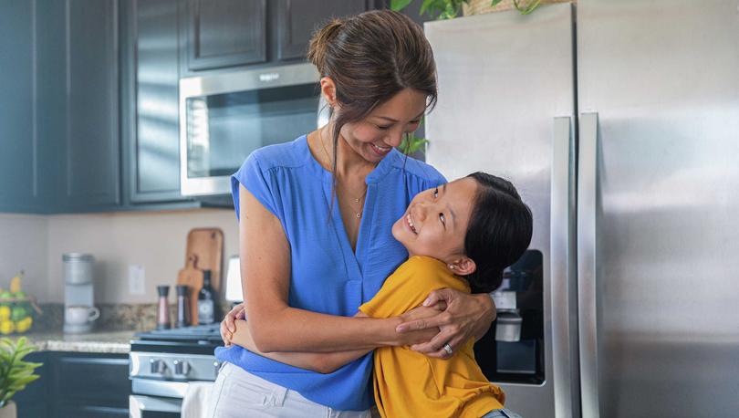 Smiling mom and daughter in the kitchen with brown cabinets.