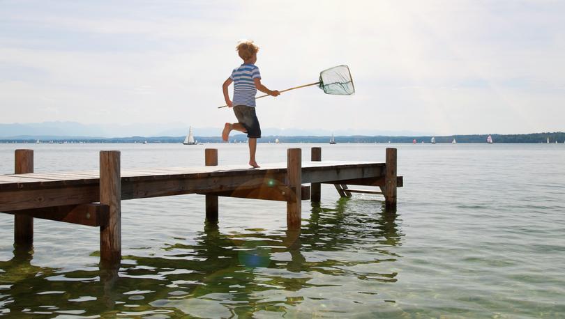 Stock photo of a boy in shorts running on a dock with a fishing net.