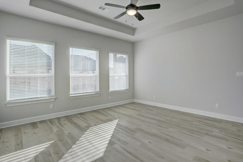 Master bedroom with three large windows that allow natural light in.