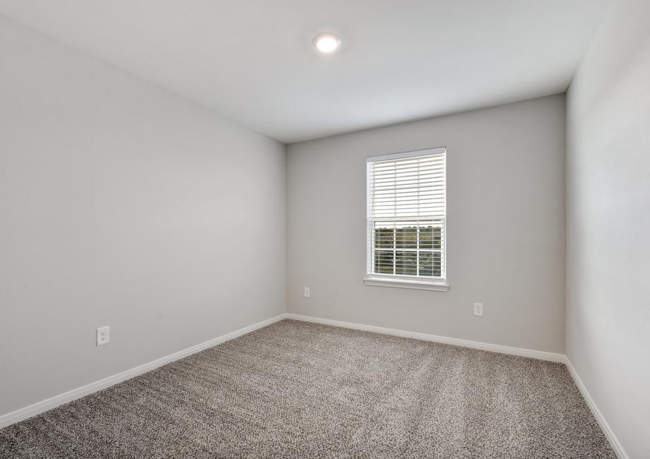 Guest bedroom with tan carpet and a window.