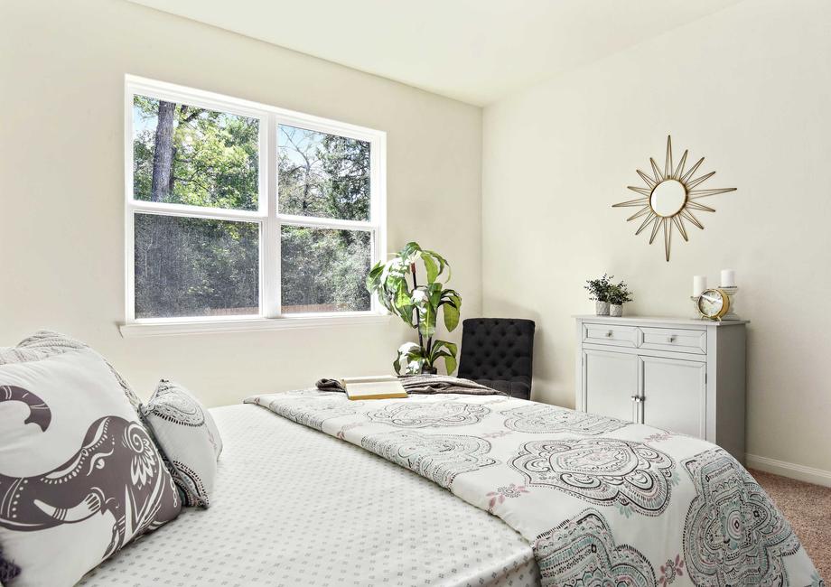 Maple staged bedroom with sun shaped clock hanging on the wall, twin bed with bluish gray comforter and pillow, and green house plant in the corner