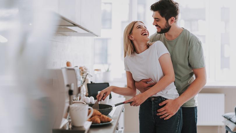 Young couple lovingly looking at each other as they cook breakfast in the kitchen.