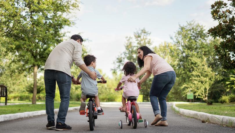 Parents teaching their two children to ride a bike.