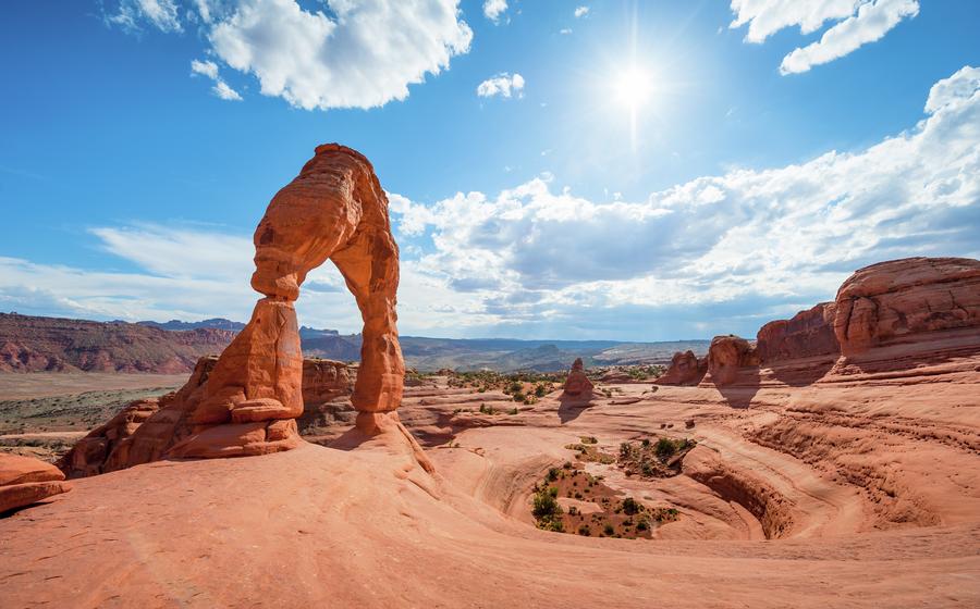 Delicate Arch at Arches National Park with sun shining in the sky.