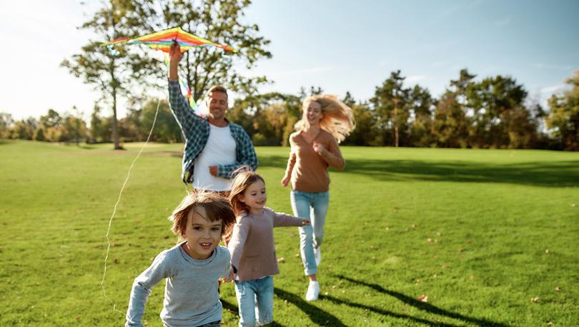 Family running in a field with a kite on a sunny day.