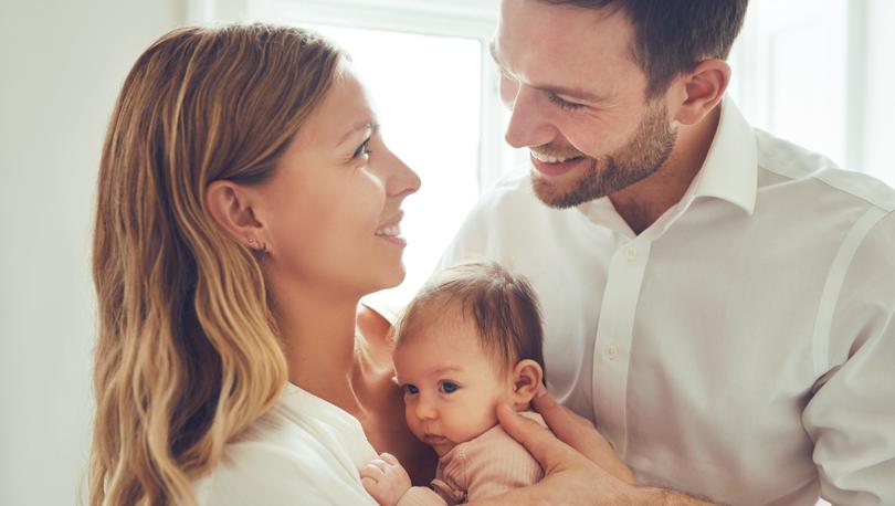 Young couple with their new baby, smiling at each other.