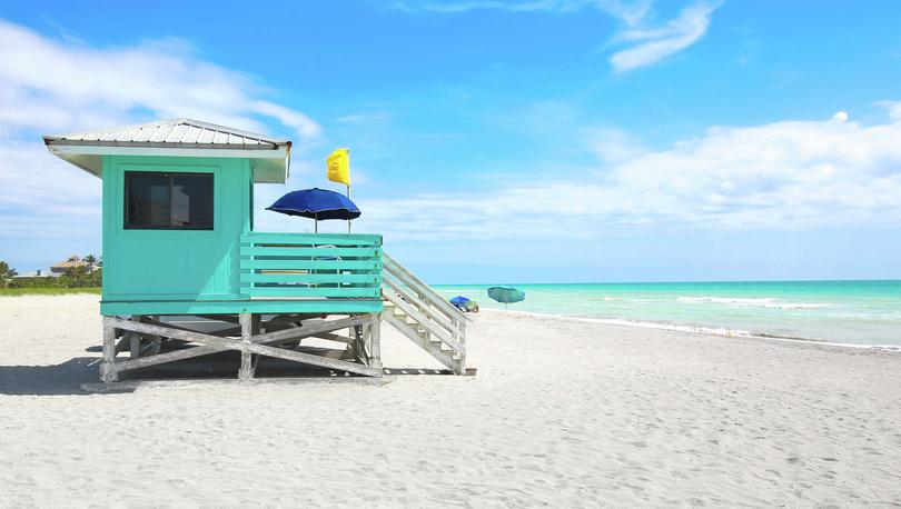 Sarasota, Florida turquoise lifeguard station with blue sun-umbrella, white sandy beach, and turquoise waters