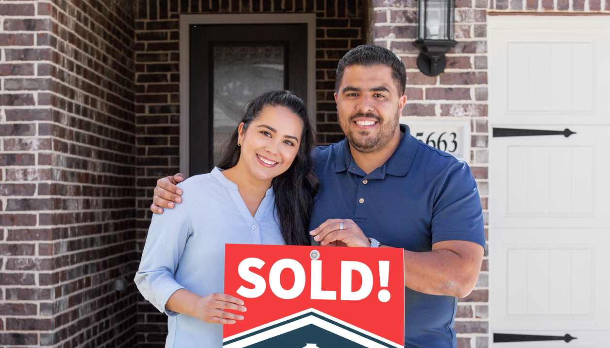 Couple standing in front of home with their sold sign