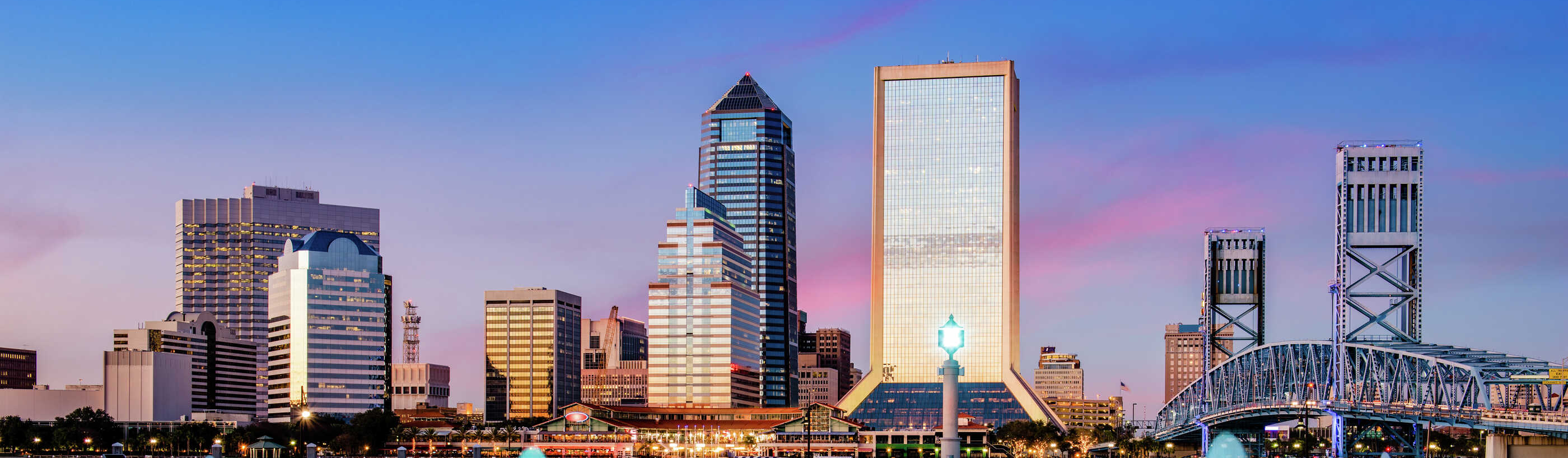 Jacksonville, Florida downtown city view at dusk with blue-light lit water features, skyscrapers in the background, and blue drawbridge