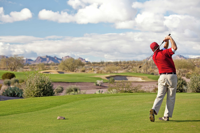Phoenix, Arizona desert landscape golf course with man teeing off, green fairways, and desert plants