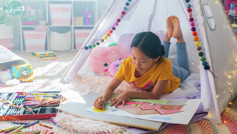 Young girl coloring with crayons in a colorful room.