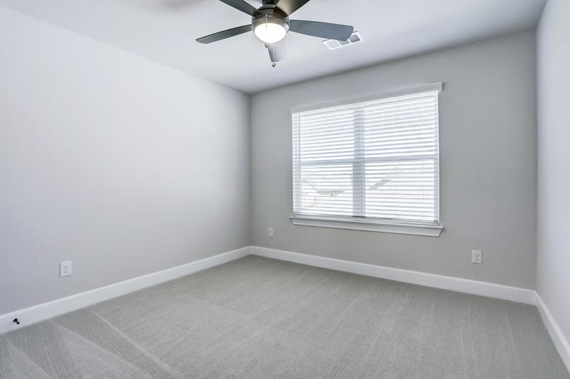Guest bedroom with soft carpet, large windows, and a ceiling fan.