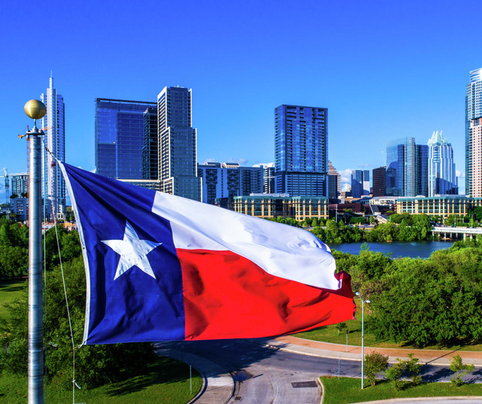 Austin, Texas Cityscape shot with numerous skyscrapers in the background, green lush park in the front and a Texas flag hanging on a flagpole