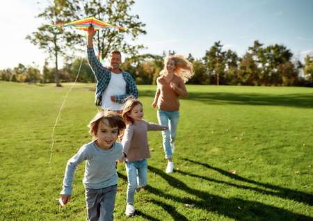 Family running in a field with a kite on a sunny day.