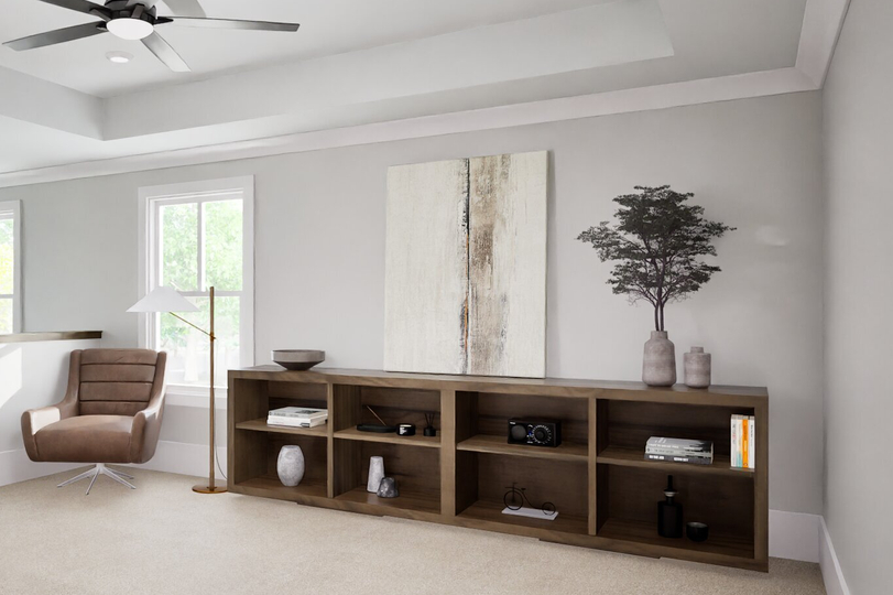 Open loft space with neutral carpet, ceiling fan, brown accent chair, wooden bookcase, and decorative accents near the staircase.