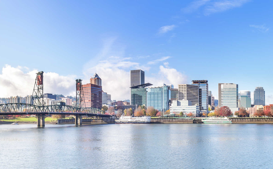 Portland, Oregon cityscape showing calm waters, railbridge, and numerous skyscrapers in the distance