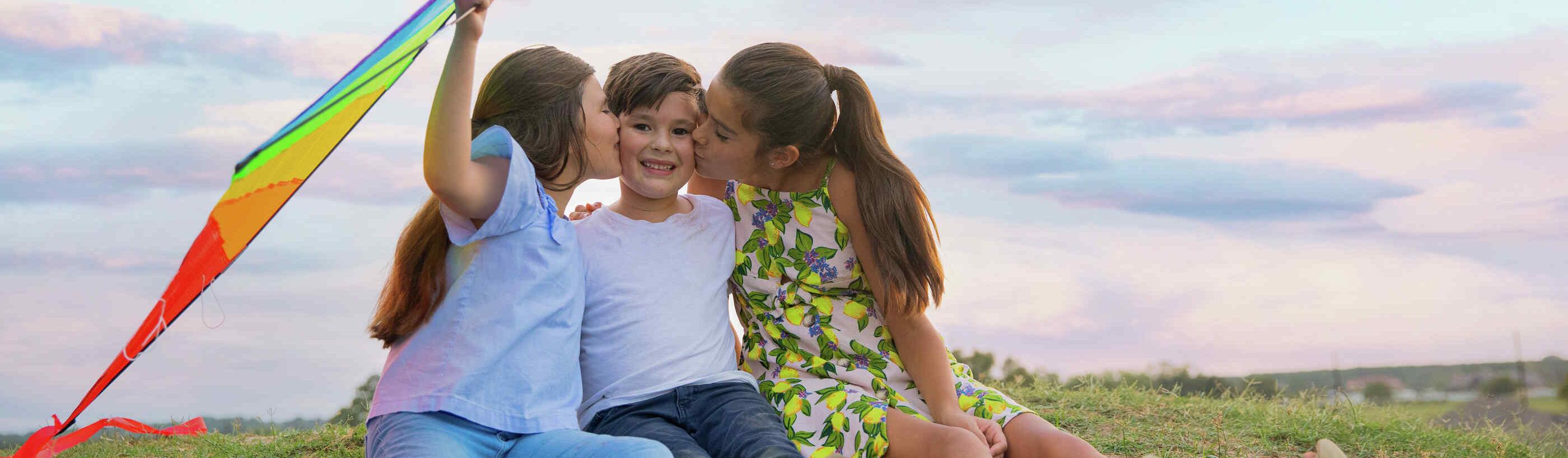 A family of young children smiling and playing outside.