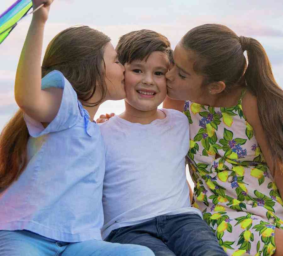 A family of young children smiling and playing outside.