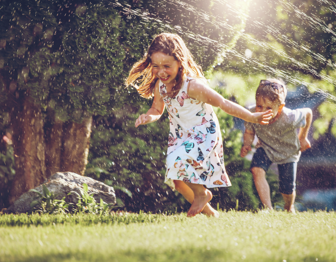 Kids running through sprinklers in a yard.