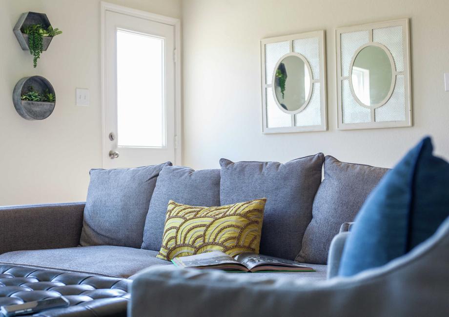 Staged living room with blueish grey couch that has a green and brown pillow on it and two framed mirrors hanging on the wall in the background