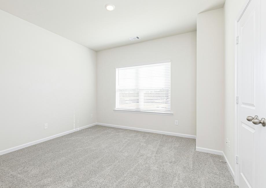 The secondary bedroom includes a closet, tan carpets and a window that lets in plenty of bright natural light