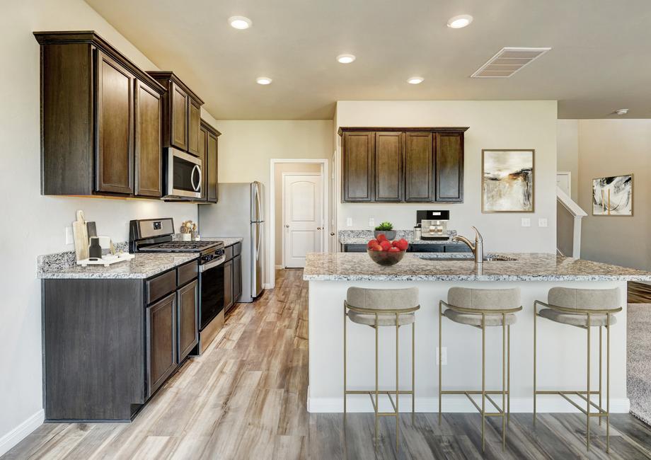 Staged kitchen with tan bar stools, brown cabinetry and light flooring.