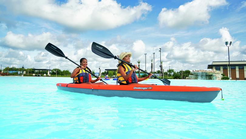 Two women in life vests paddle across the lagoon in a kayak.