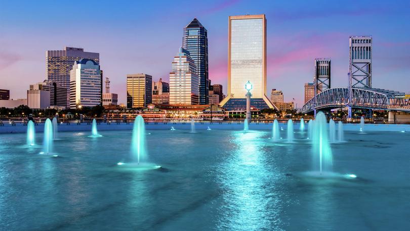 Jacksonville, Florida downtown city view at dusk with blue-light lit water features, skyscrapers in the background, and blue drawbridge