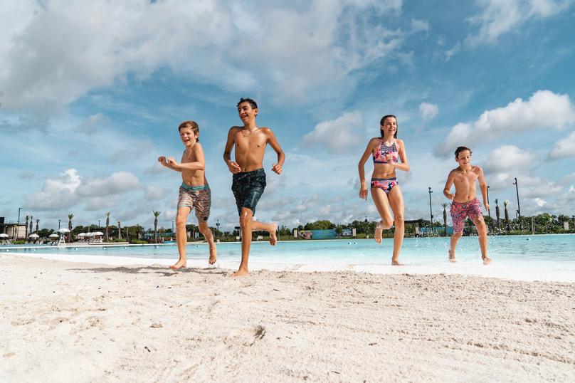 Three pre-teen boys and one girl happily run onto the sandy beach from the crystal lagoon.