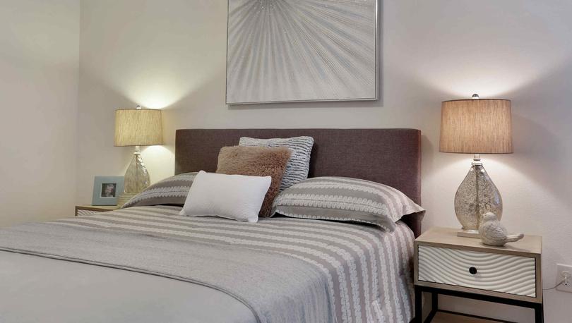 Bed with gray linens, side tables with lamps and a decorative wall hanging.