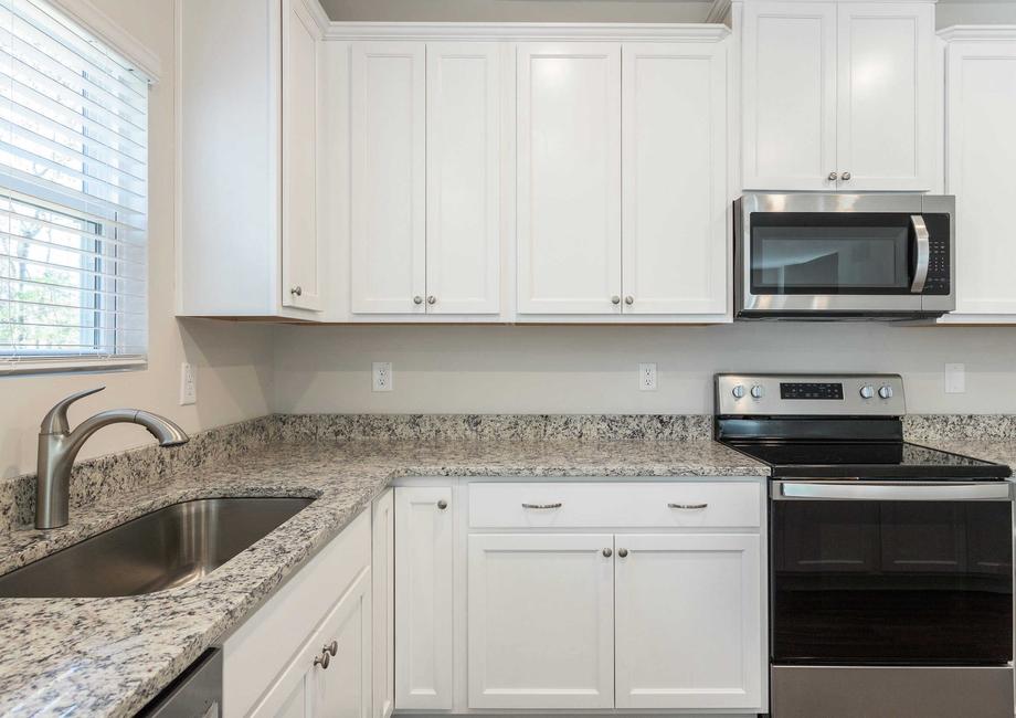 Kitchen with stainless steel appliances, granite countertops and white cabinetry with hardware.
